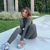 Person in grey fitted athletic long sleeve skiing jumpsuit with silver sneakers sitting on concrete